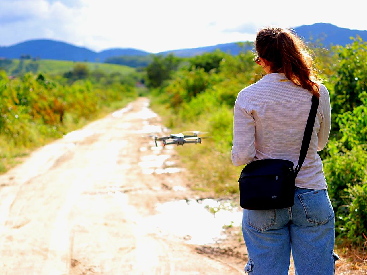Drone pousado em estrada de terra, pronto para decolar, com reservatório e montanhas ao fundo